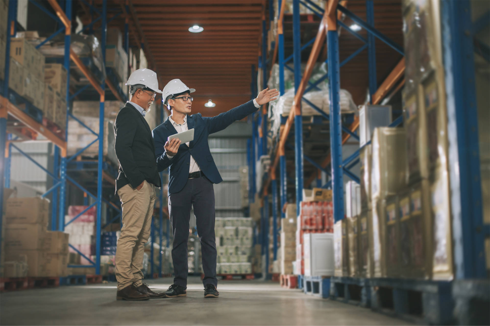 Supply chain managers looking at stock in a warehouse wearing hard hats.