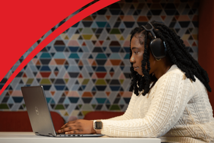 A woman is typing on a laptop while wearing a pair of over-the-ear headphones.