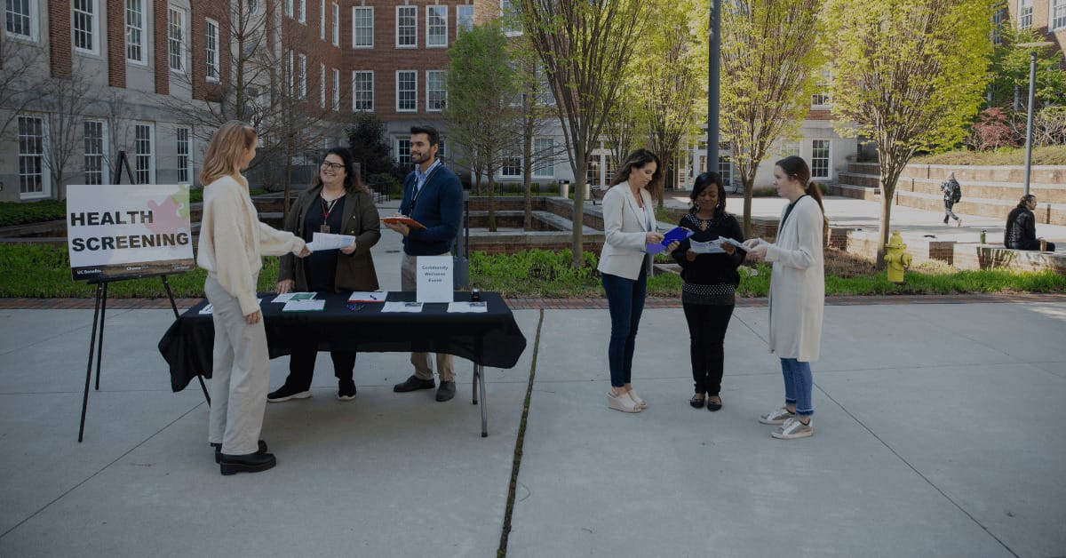 A group of people standing outside next to a table during a public health screening event.