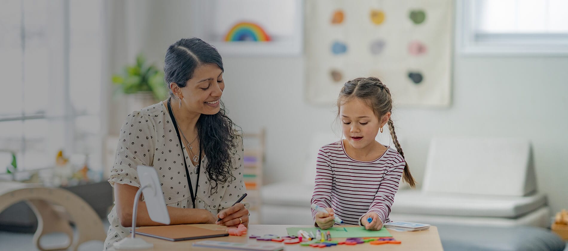 Behavior analyst engaging with a child in classroom setting. The child is drawing a picture with a blue marker.