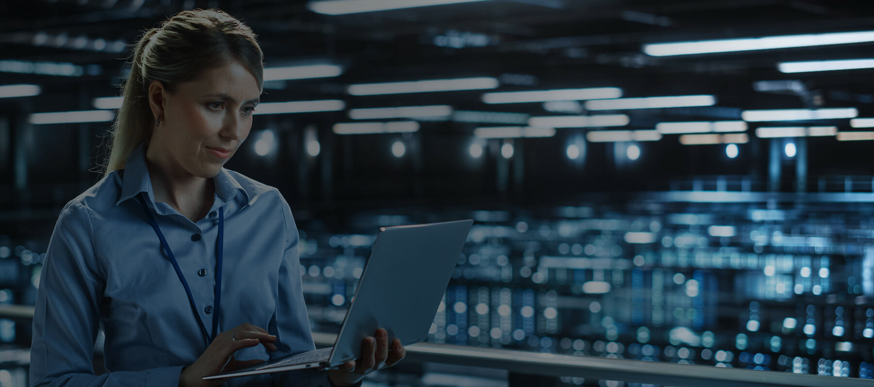 Information systems specialist monitoring servers on a laptop in a data center.