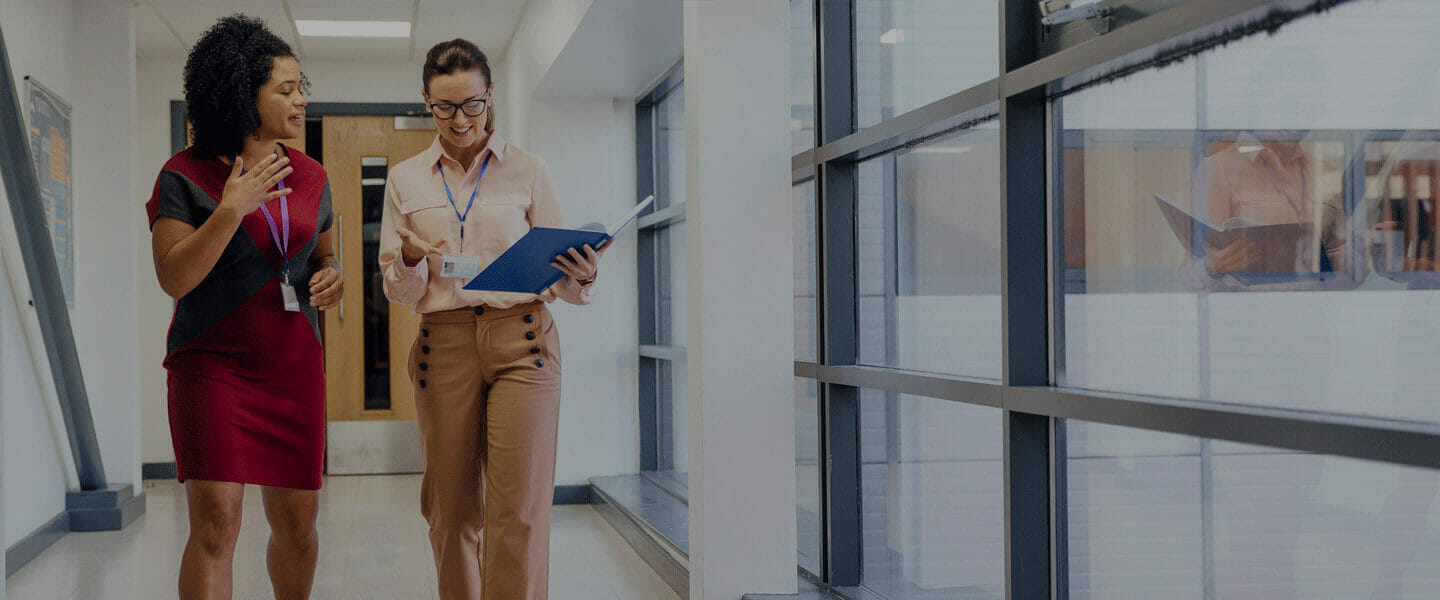 Two school administrators walking through a hallway discussing documents.