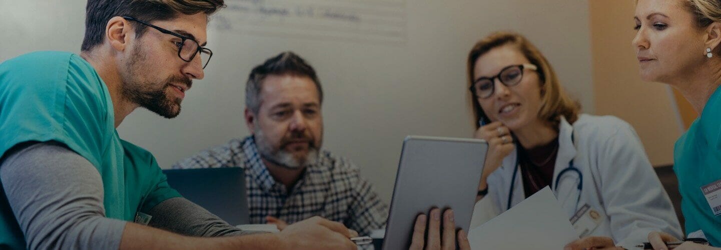 Four Health Informatics Professionals looking at a tablet while sitting down in a meeting room.