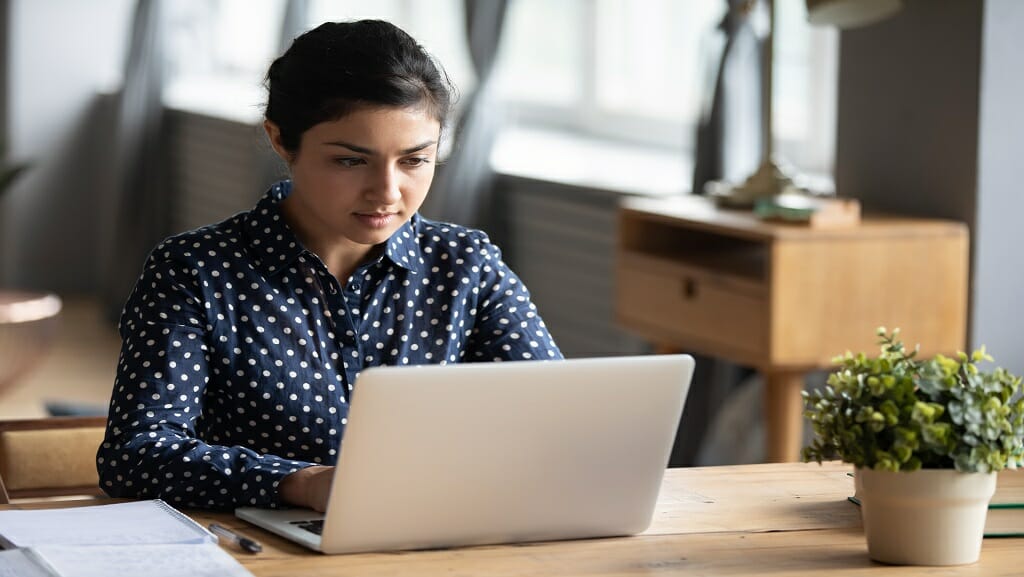 Focused Indian girl studying on laptop at home