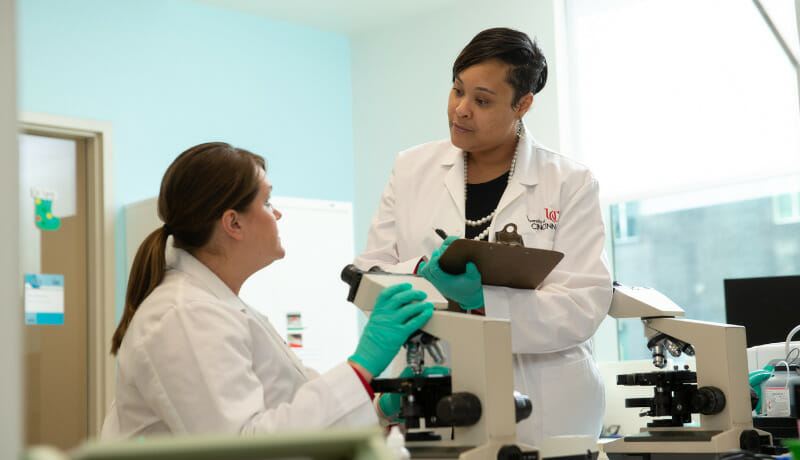 A student looking into a microscope addressing a leader from a lab table